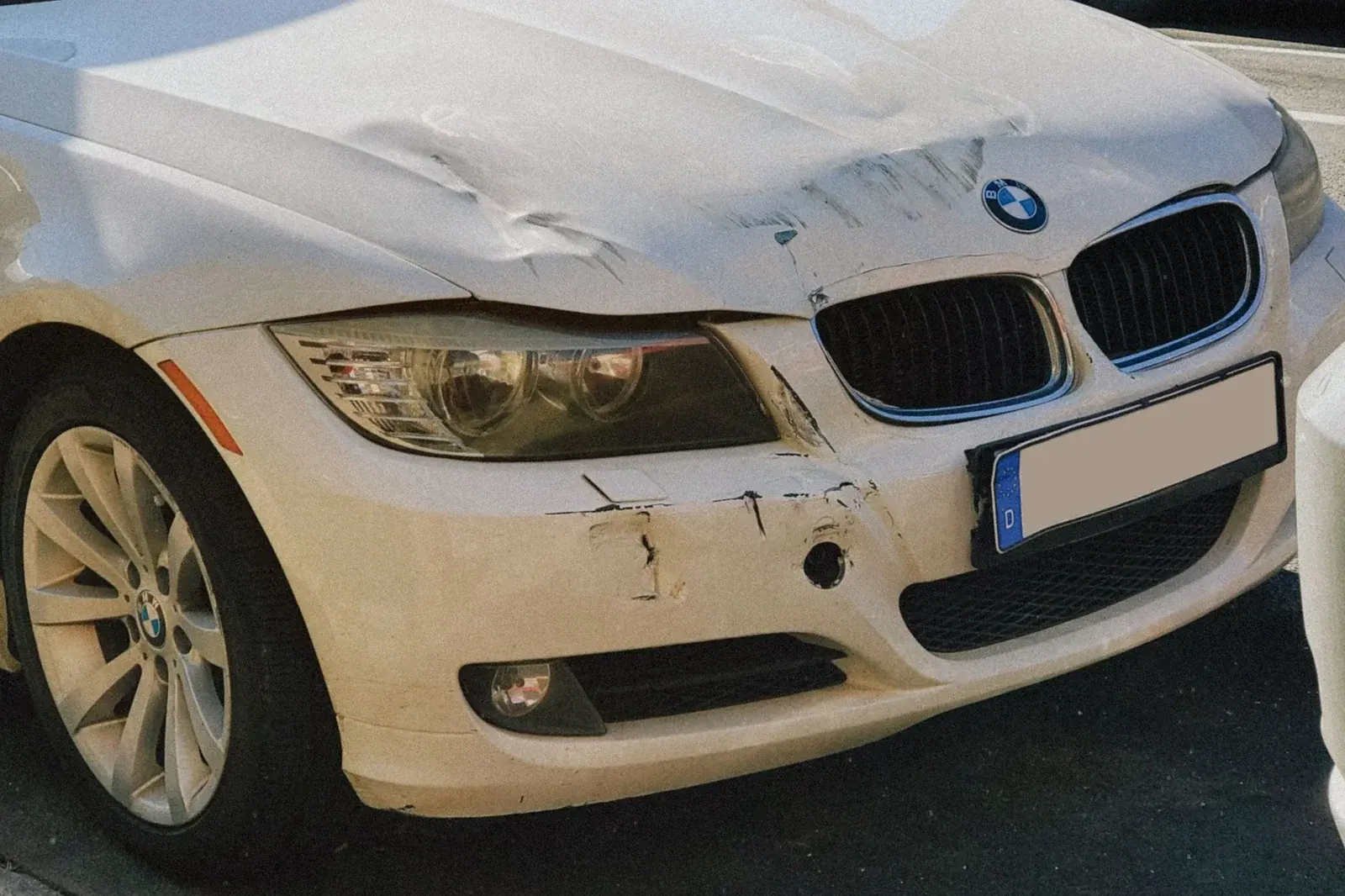 Dented hood and scuffed front bumper on a white sedan